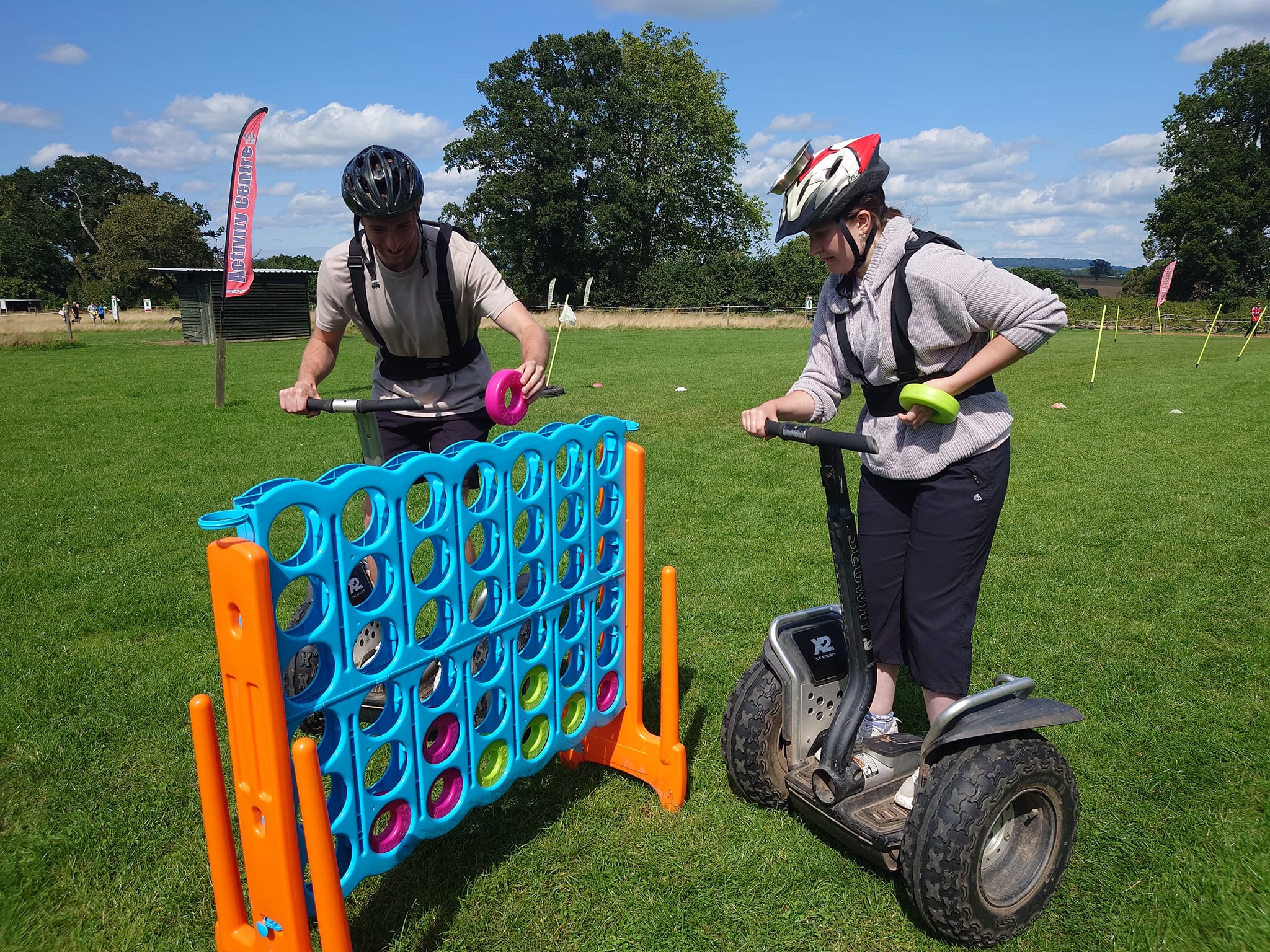 Two helmeted riders playing giant Connect Four on Segways at Escot